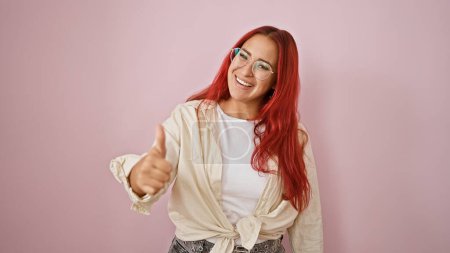 Photo for Joyous young redhead woman grinning, confidently gives cool ok sign with thumb up, standing over isolated pink background - Royalty Free Image