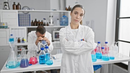 Photo for Two determined scientists, a man and woman, work together in a lab, portraying serious concentration with arms crossed gesture - Royalty Free Image