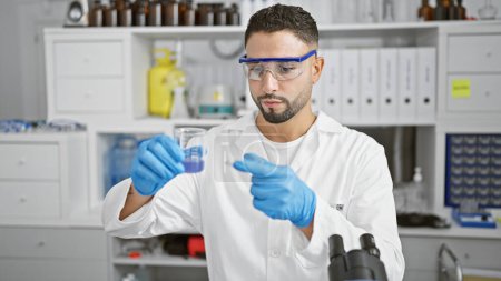 Photo for A bearded man in lab coat examines a test tube in a modern laboratory, showcasing a professional research environment. - Royalty Free Image
