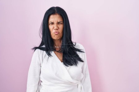 Téléchargez les photos : Femme hispanique mature debout sur fond rose joues gonflées avec un visage drôle. bouche gonflée d'air, expression folle. - en image libre de droit
