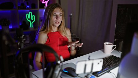 Téléchargez les photos : Une jeune femme s'engage avec un public lors de l'enregistrement d'une vidéo dans une salle de jeux éclairée au néon la nuit. - en image libre de droit