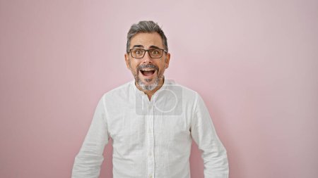 Oh wow! grey-haired young hispanic man with surprising expression, amazed and standing over an isolated pink background, totally incredible. handsome male with open mouth and glasses.