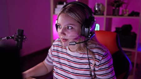 Téléchargez les photos : Focalisé femme caucasienne portant des écouteurs dans une salle de jeu colorée avec microphone et PC la nuit. - en image libre de droit