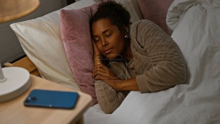 Téléchargez les photos : Une femme paisible dormant dans une chambre confortable avec un smartphone sur la table de chevet. - en image libre de droit