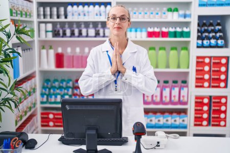 Photo for Young caucasian woman working at pharmacy drugstore praying with hands together asking for forgiveness smiling confident. - Royalty Free Image