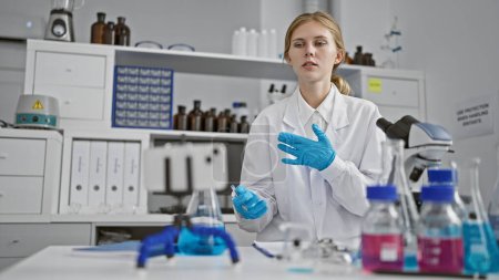 Foto de Mujer rubia científica con guantes azules trabaja en un laboratorio con equipo químico. - Imagen libre de derechos