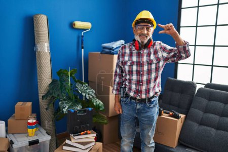 Photo for Senior man with safety glasses and hardhat radiates confidence in his new home, gesturing a small sign with his fingers - a handyman's personal measure of success. - Royalty Free Image