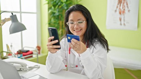 Foto de Mujer joven china médico de compras con teléfono inteligente y tarjeta de crédito en la clínica - Imagen libre de derechos