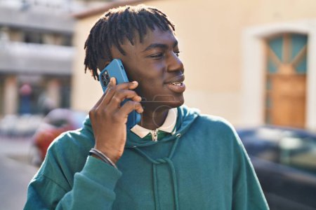 Téléchargez les photos : Afro-Américain souriant confiant parler sur le smartphone à la rue - en image libre de droit