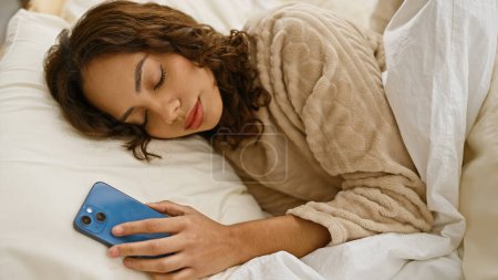 Photo for A woman sleeps in a bed holding a smartphone, suggesting a connection to technology even in restful moments. - Royalty Free Image