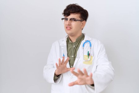 Photo for Young non binary man wearing doctor uniform and stethoscope afraid and terrified with fear expression stop gesture with hands, shouting in shock. panic concept. - Royalty Free Image