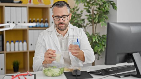 Photo for Grey-haired man doctor eating salad while work at the clinic - Royalty Free Image