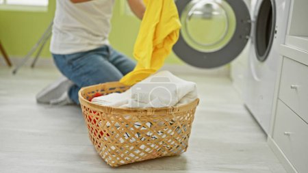 Foto de Un joven arrodillado mientras lavaba la ropa en una habitación iluminada, añadiendo vitalidad y un toque doméstico. - Imagen libre de derechos