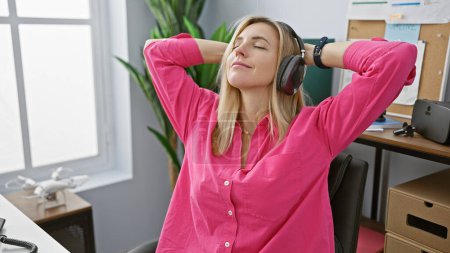 Photo for Relaxed young woman enjoying music with headphones in a bright office setting - Royalty Free Image