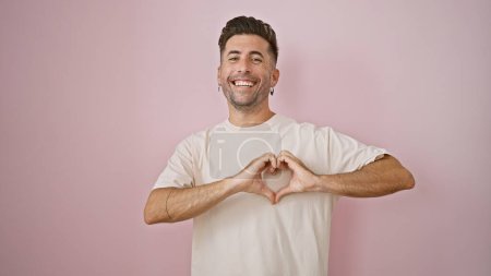 Foto de Sonriente joven hispano hace un gesto de confianza en el corazón con las manos sobre un fondo rosa aislado, mostrando una alegre confianza en el estilo de vida casual de la moda - Imagen libre de derechos