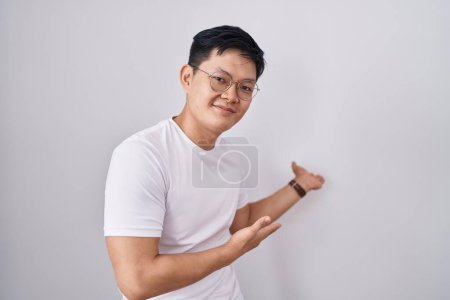 Foto de Joven asiático hombre de pie sobre blanco fondo invitando a entrar sonriendo natural con la mano abierta - Imagen libre de derechos