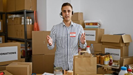 Un joven hispano llamado Alex está en un almacén con cajas, auriculares y letreros de donación, representando el trabajo voluntario..