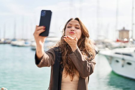 Foto de Joven hermosa mujer hispana sonriendo confiada haciendo selfie por el teléfono inteligente en la playa - Imagen libre de derechos