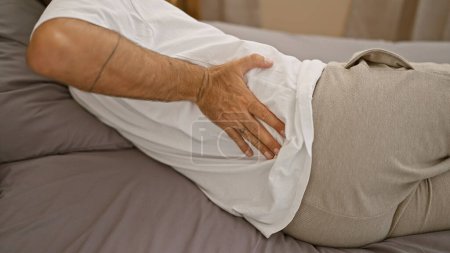 Leidender Mann, Hände berühren seinen verletzten Rücken, liegen auf dem Bett im Schlafzimmer, geweckt von schmerzhaften Rückenschmerzen