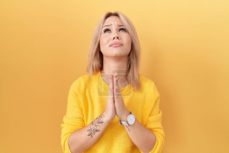 Photo for Young caucasian woman wearing yellow sweater begging and praying with hands together with hope expression on face very emotional and worried. begging. - Royalty Free Image