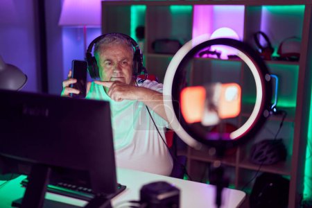 Photo for Middle age grey-haired man streamer having video call holding smartphone at gaming room - Royalty Free Image