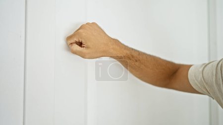 A close-up of a man's clenched fist knocking on a white door, emphasizing anticipation and arrival in a home setting.