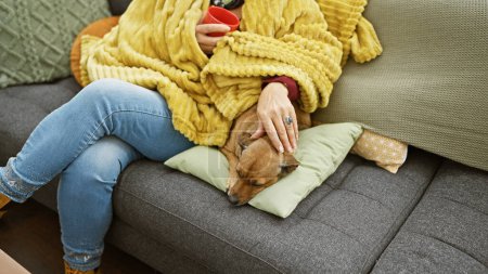 Téléchargez les photos : Une femme se détend sur un canapé, caressant un chien endormi, entouré d'une couverture jaune et d'oreillers colorés dans un salon confortable. - en image libre de droit