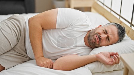 Téléchargez les photos : Homme aux cheveux gris souffrant de maux d'estomac couché sur le lit dans la chambre - en image libre de droit
