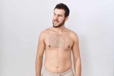 Photo for Young hispanic man standing shirtless over white background looking away to side with smile on face, natural expression. laughing confident. - Royalty Free Image