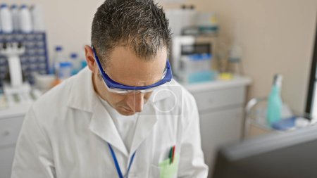 Foto de Hombre hispano en labcoat enfocado en el trabajo en un ambiente de laboratorio, encarnando profesionalismo y servicio de salud. - Imagen libre de derechos