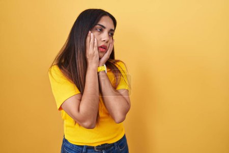 Téléchargez les photos : Jeune femme arabe debout sur fond jaune mains fatiguées couvrant le visage, la dépression et la tristesse, bouleversé et irrité par le problème - en image libre de droit
