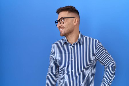 Téléchargez les photos : Homme hispanique à la barbe portant des lunettes regardant de côté avec le sourire sur le visage, expression naturelle. riant confiant. - en image libre de droit