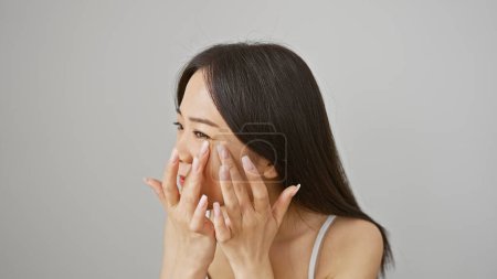 Photo for A young asian woman smiles subtly, touching her face with her hands, against a white backdrop - Royalty Free Image