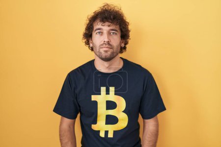 Photo for Hispanic young man wearing bitcoin t shirt relaxed with serious expression on face. simple and natural looking at the camera. - Royalty Free Image