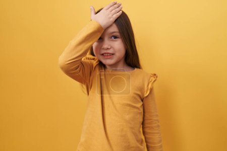Surprised adorable hispanic girl, forgot crucial error, hand on head in regret. stands isolated on yellow background, memory fail, blunder recalled!