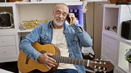 A middle-aged man holding a guitar and talking on the phone in a music-filled room with instruments.