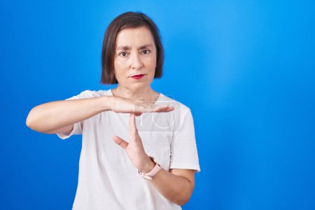 Photo for Middle age hispanic woman standing over blue background doing time out gesture with hands, frustrated and serious face - Royalty Free Image