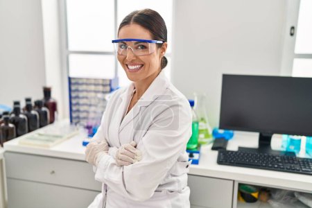 Photo for Young beautiful hispanic woman scientist smiling confident sitting with arms crossed gesture at laboratory - Royalty Free Image