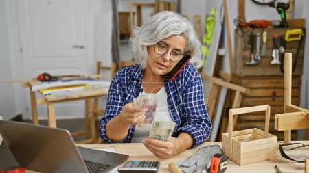 Téléchargez les photos : Une femme aux cheveux gris examine des billets de banque en zloty dans un atelier de menuiserie. - en image libre de droit