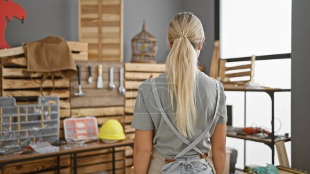 Téléchargez les photos : Femme blonde dans l'atelier entourée d'outils et de bois, incarnant la créativité et l'artisanat. - en image libre de droit