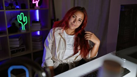 Vivacious young redhead woman streamer, smiling as she skillfully plays a vibrant game, effortlessly streaming from her homey gaming room, basking in the soft glow of her computer