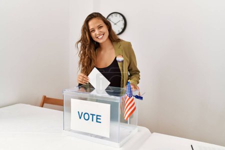Foto de Joven mujer hispana hermosa mesa electoral presidente poniendo voto en caja en colegio electoral - Imagen libre de derechos