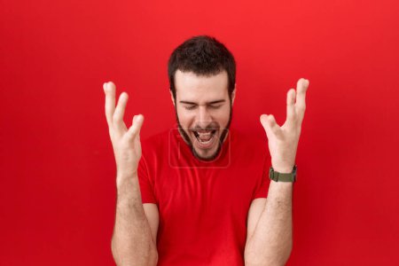 Téléchargez les photos : Jeune homme hispanique portant t-shirt rouge occasionnel célébrant fou et fou de succès avec les bras levés et les yeux fermés hurlant excité. concept gagnant - en image libre de droit