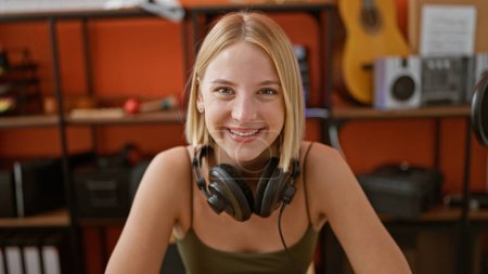 Téléchargez les photos : Jeune femme blonde musicienne portant des écouteurs souriant au studio de podcast - en image libre de droit