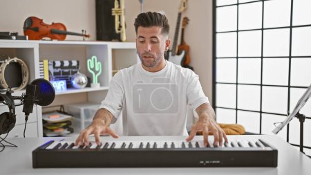 Téléchargez les photos : Beau jeune homme hispanique, artiste musical, jouant passionnément de la mélodie acoustique au piano lors d'un appel vidéo captivant. plonger dans le monde de la musique à l'intérieur dans un studio dynamique! - en image libre de droit