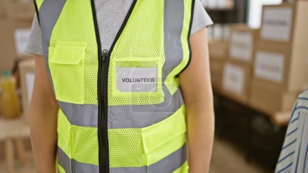 Photo for Beautiful blonde young woman volunteer, standing in reflective vest, serving in community charity center with altruism and unity - Royalty Free Image