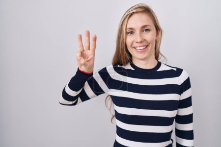 Téléchargez les photos : Jeune femme caucasienne portant pull marine décontracté montrant et pointant vers le haut avec les doigts numéro trois tout en souriant confiant et heureux. - en image libre de droit