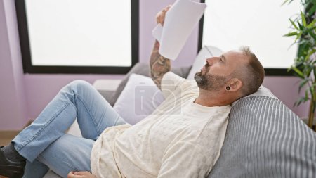 Foto de El tiempo caliente tormento, joven que se abanica con documentos, sufriendo en una habitación sin viento, sentado en el sofá en casa - Imagen libre de derechos