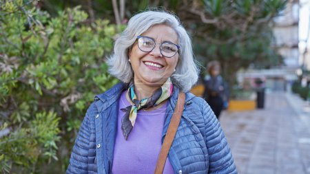 Foto de Mujer madura sonriente con el pelo gris usando gafas al aire libre en un parque de la ciudad - Imagen libre de derechos
