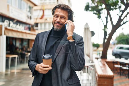 Foto de Hombre de mediana edad hablando en el teléfono inteligente beber café en la calle - Imagen libre de derechos